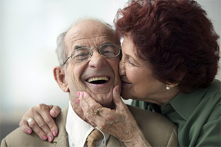 Senior woman kisses cheek of smiling senior man